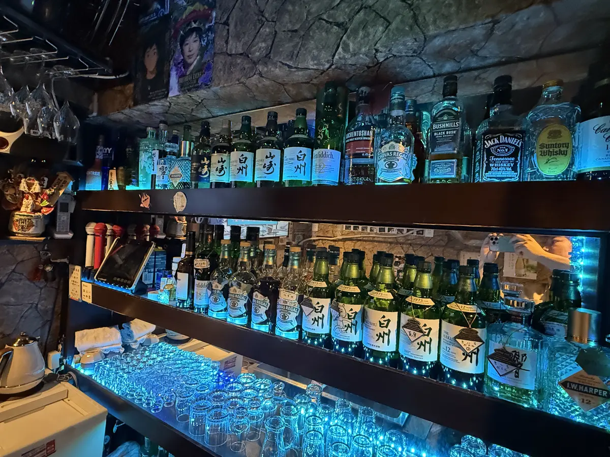 青いライトに照らされたBAR NOMENOMEのボトル棚とグラス